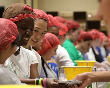 A line of volunteers in red hairnets prepare food.