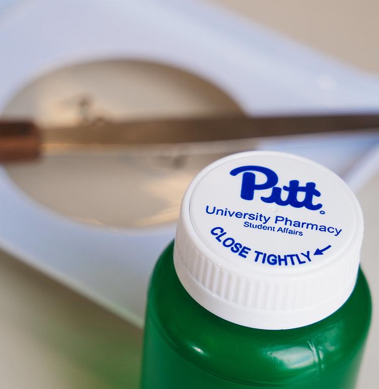 Green pill bottle with white lid that reads "Pitt."