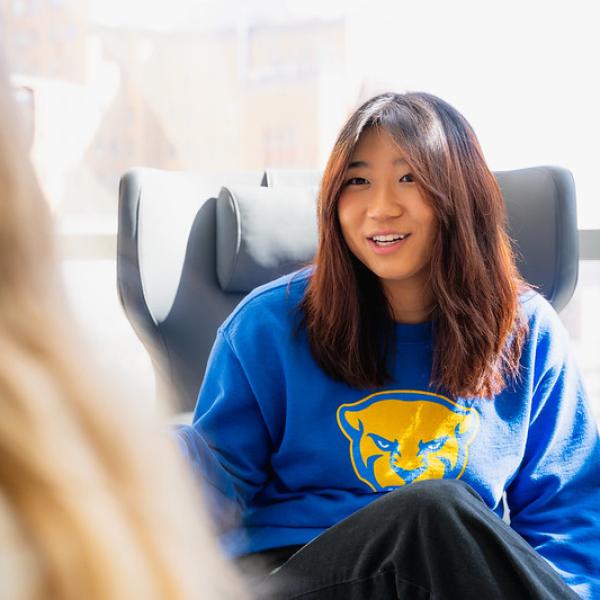 Woman sitting in chair in a Pitt sweatshirt.