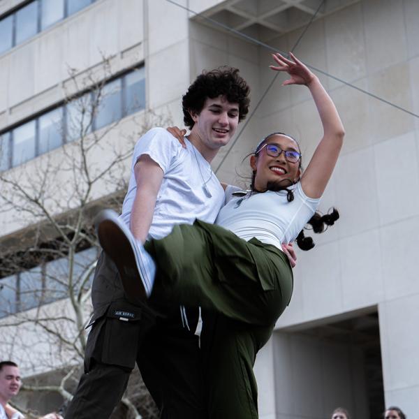 Two students both in white t-shirts and green pants dancing.