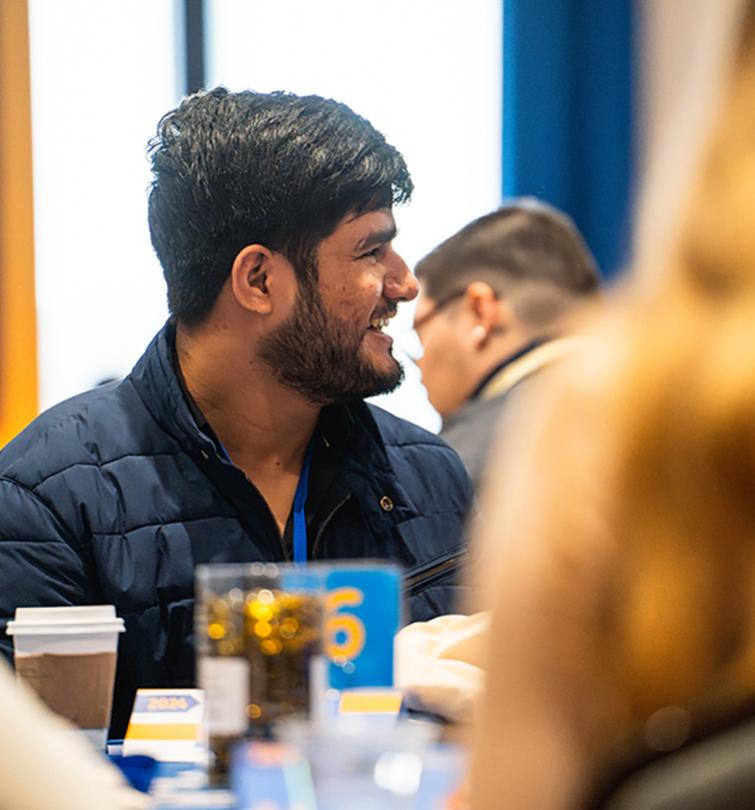 Student with dark short hair and dark facial hair smiling.