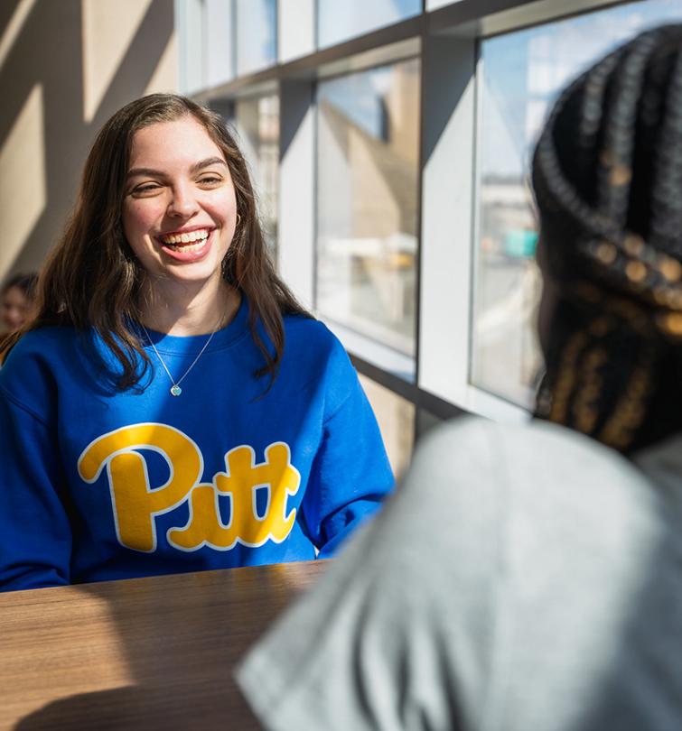 Woman smiling and laughing in a blue crewneck sweatshirt.