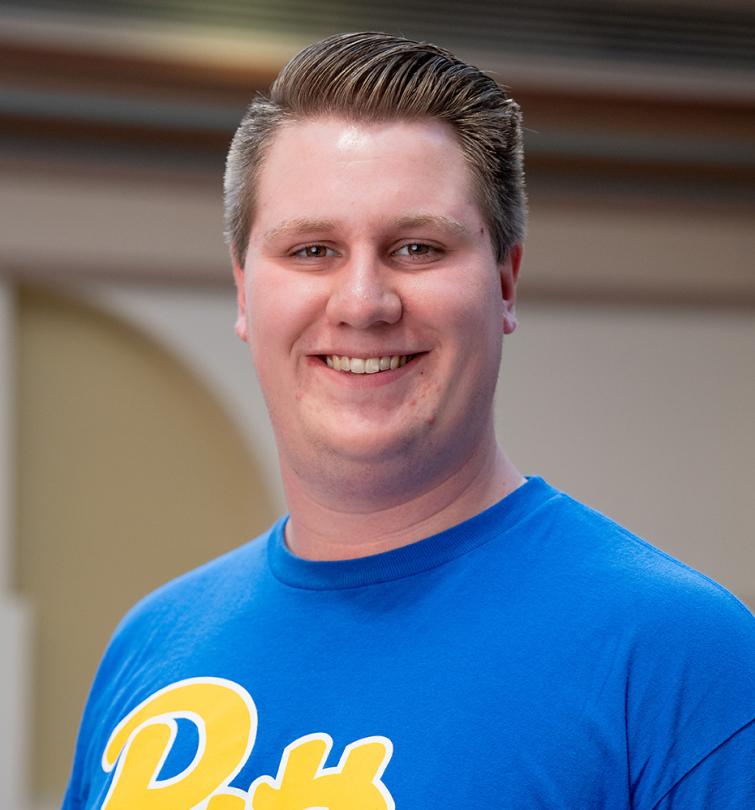 A man with short blonde hair smiling in a blue tshirt.