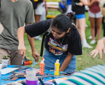 A student with long dark hair in a black t-shirt rolling paint onto a project.