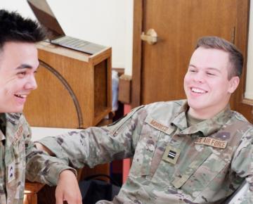 Two men in military uniforms laughing and seated.