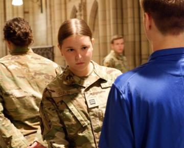 Female student in a military uniform inspecting a male student's uniform.