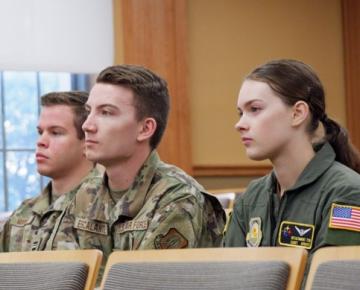 Three students in military uniforms sitting in an auditorium.