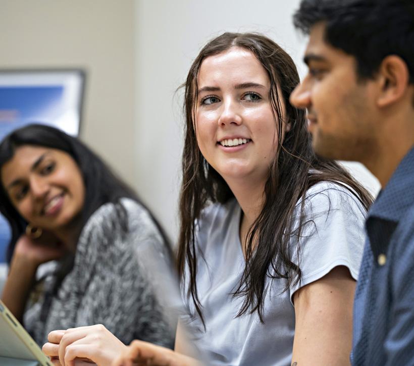 Students seated smiling at each other in a classroom.