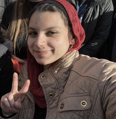 Woman in a red hood holding up peace sign.
