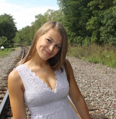 Woman with long blonde hair smiling in a light blue sleeveless top.