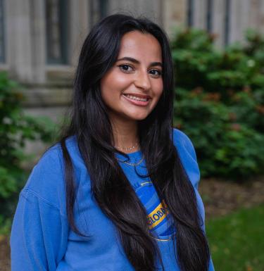 Headshot of a smiling woman outdoors with long black shiny hair wearing a blue GLobal Ties crewneck shirt.