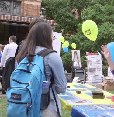 A student looks at a table decorated with a tablecloth and balloons outdoors.