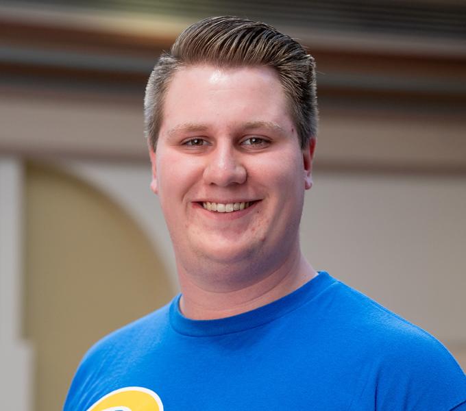 A man with short blonde hair smiling in a blue shirt.