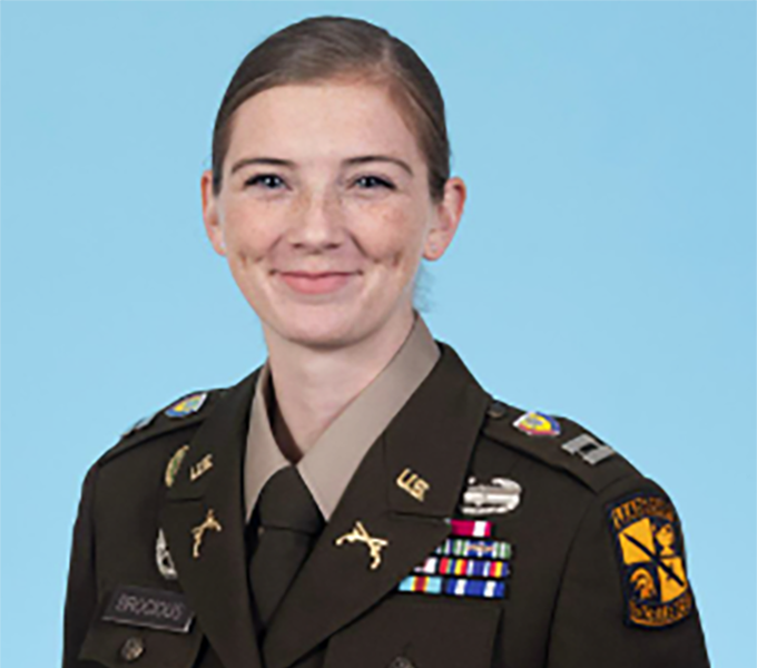 Woman in military uniform smiling in front of a blue background.