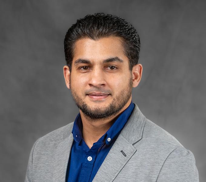 Photo of a man smiling in a blue shirt and grey suit.