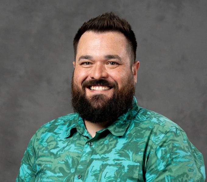 Photo of a man with dark facial hair smiling in a green polo shirt.