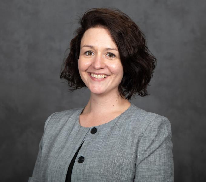 Headshot of smiling woman in a gray blouse with short brown hair.