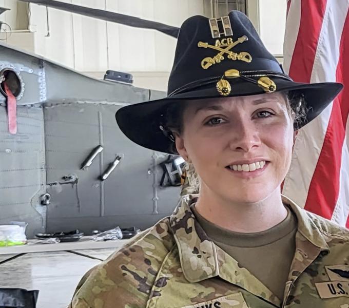 Woman in a military uniform smiling standing in front of the American flag.