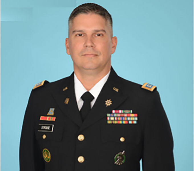 Man in a military uniform standing in front of a light blue background.