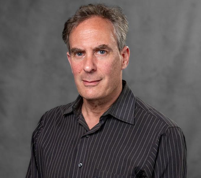 A man with grey hair in a brown pinstripe button down shirt.