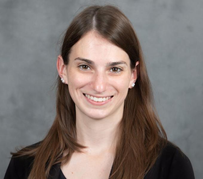 Headshot of a smiling woman with long straight brown hair in a black shirt.