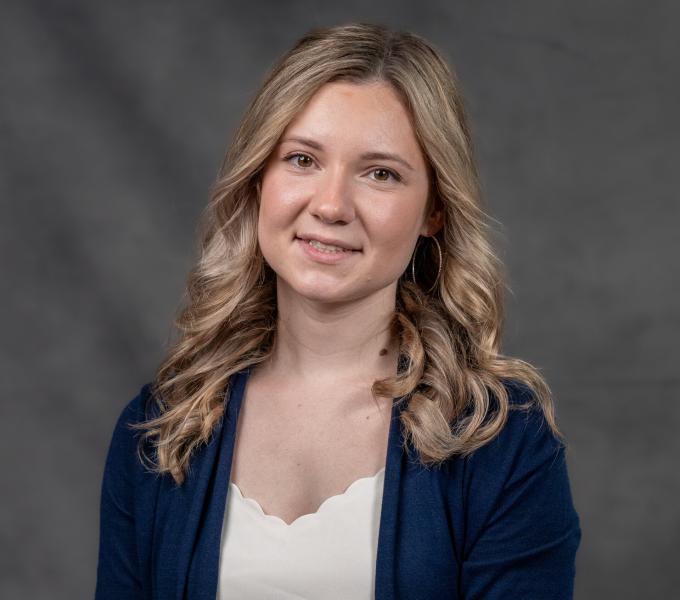 Headshot of a blonde woman in a white satin shirt and navy blue cardigan.